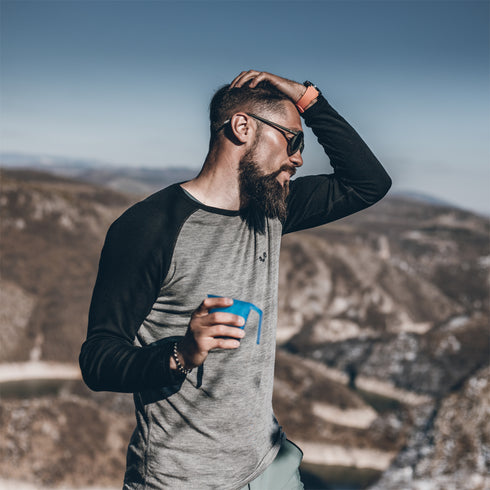 Mann mit Sonnenbrille in den Bergen trägt einen Merinoshirt mit schwarzen Ărmeln